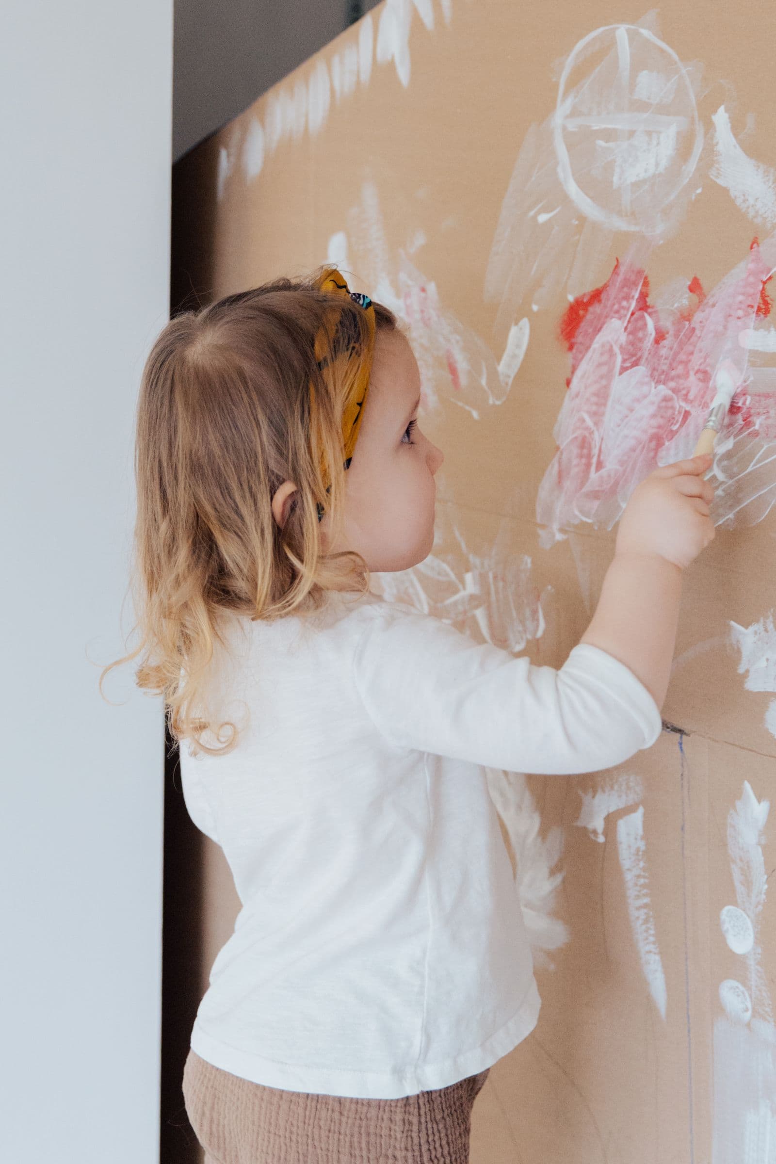 A young child concentrating on a painting, hands and sleeves covered in colour.