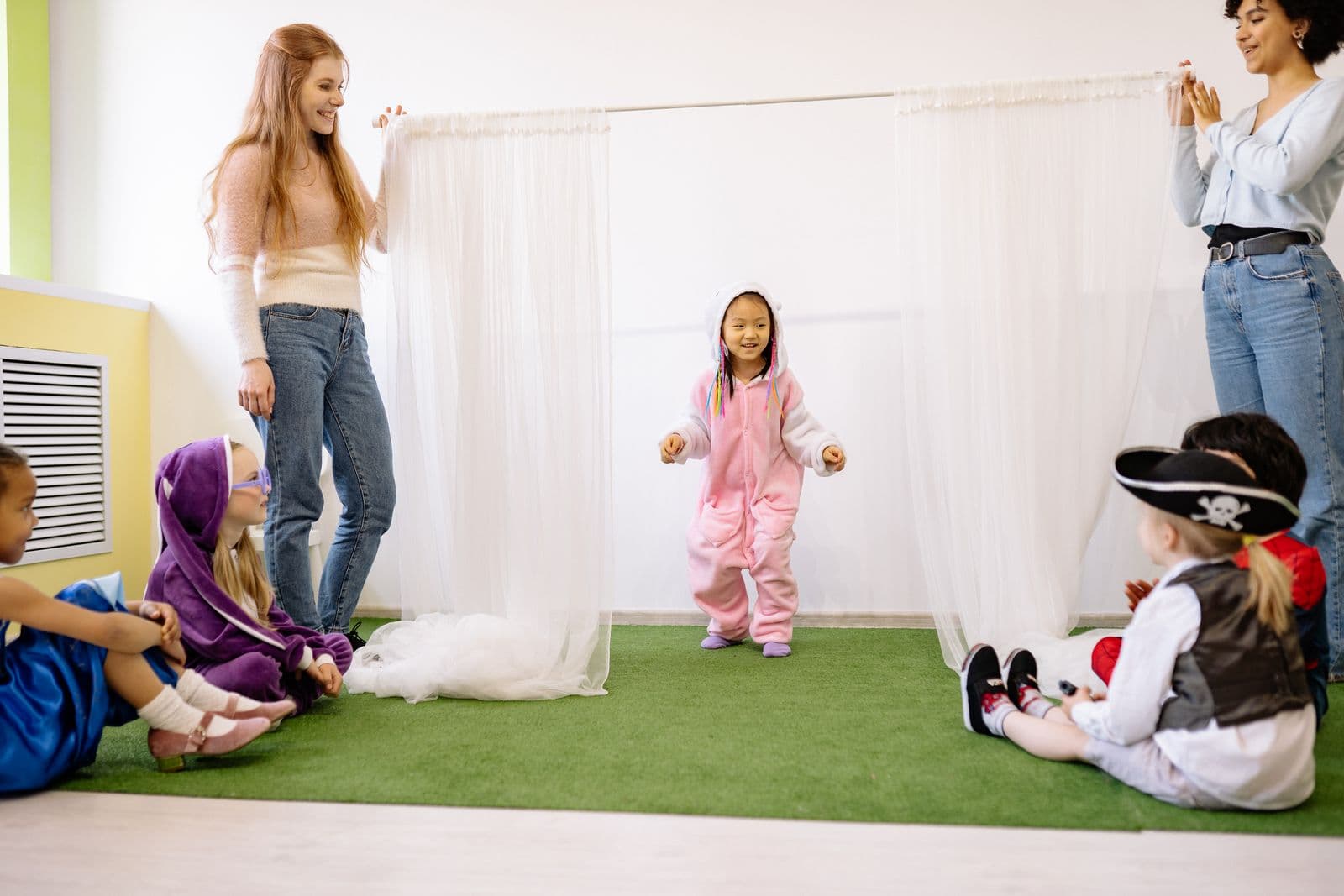 Children and two adults building a den out of fabric draped over a frame.