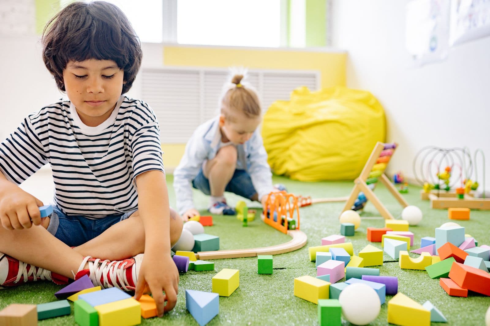 A boy and a girl sitting on the floor building with wooden blocks.
