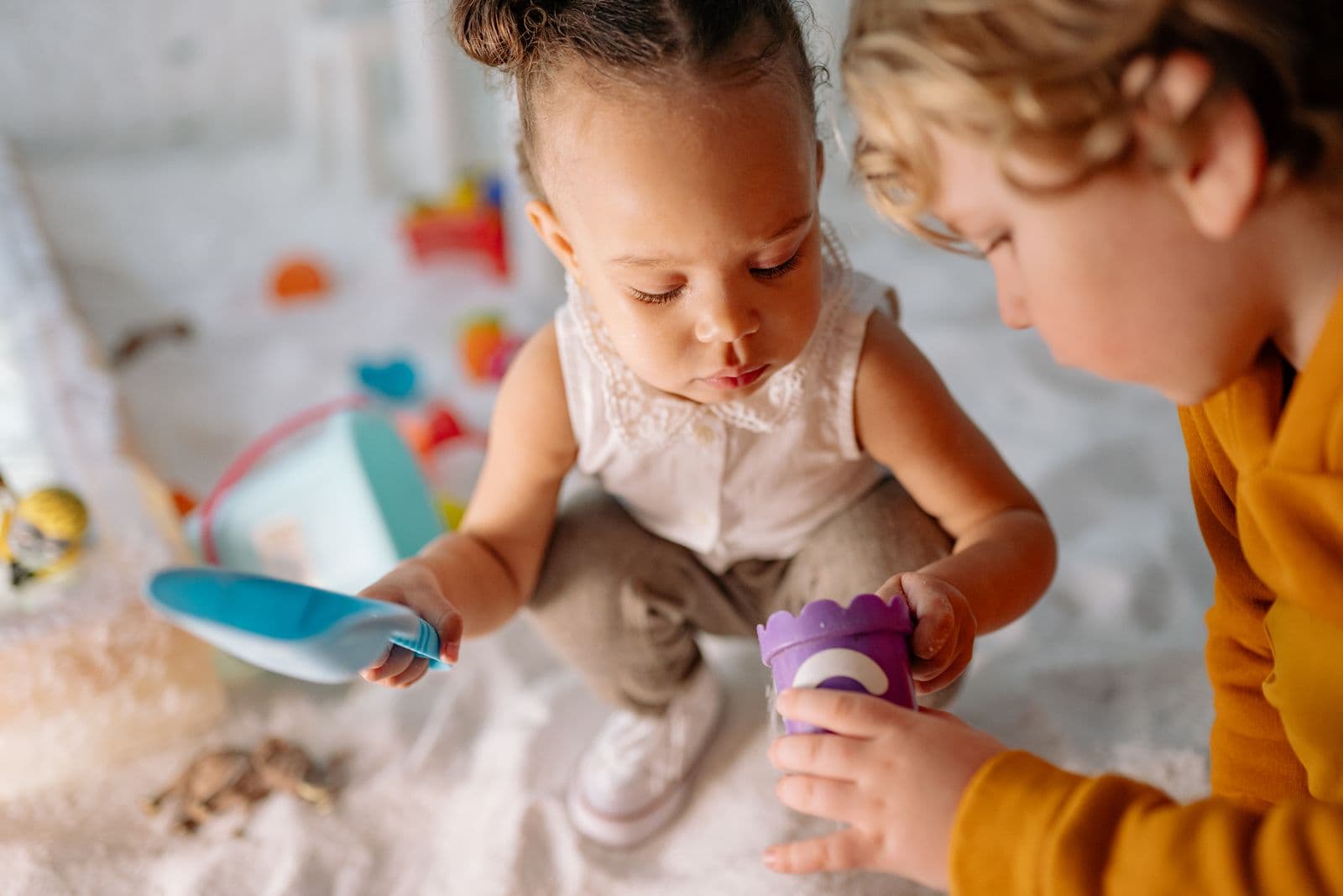 Two small children examining a toy closely together, heads bent over it.