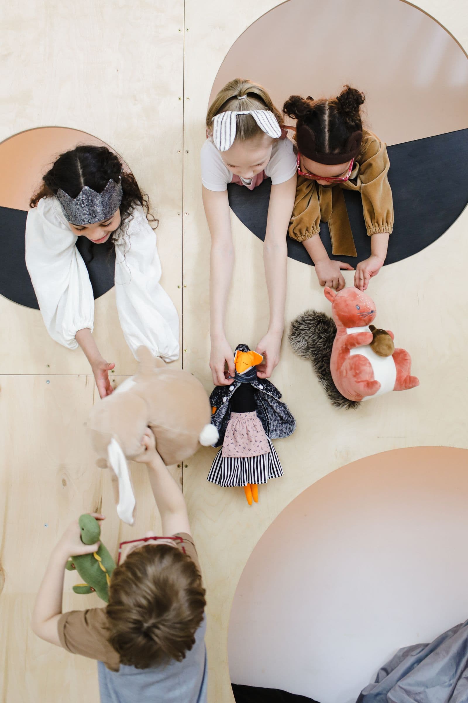 Overhead view of a child arranging a doll and small toys on a wooden table.