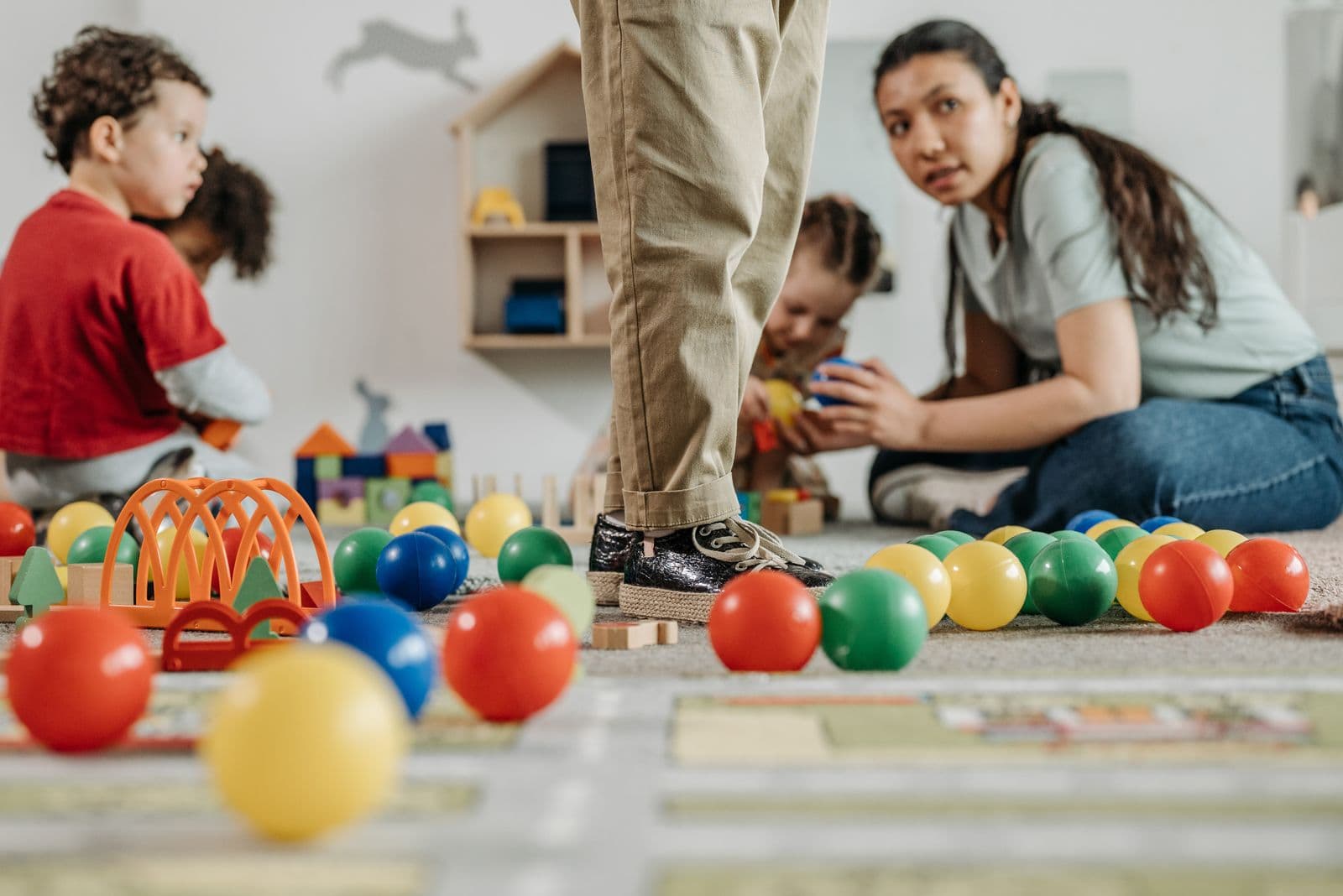 An educator on the floor with a group of preschool children, playing with coloured balls.