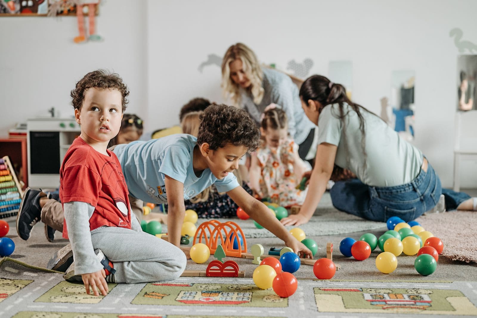 Toddlers sitting on a play mat surrounded by coloured balls and soft toys.
