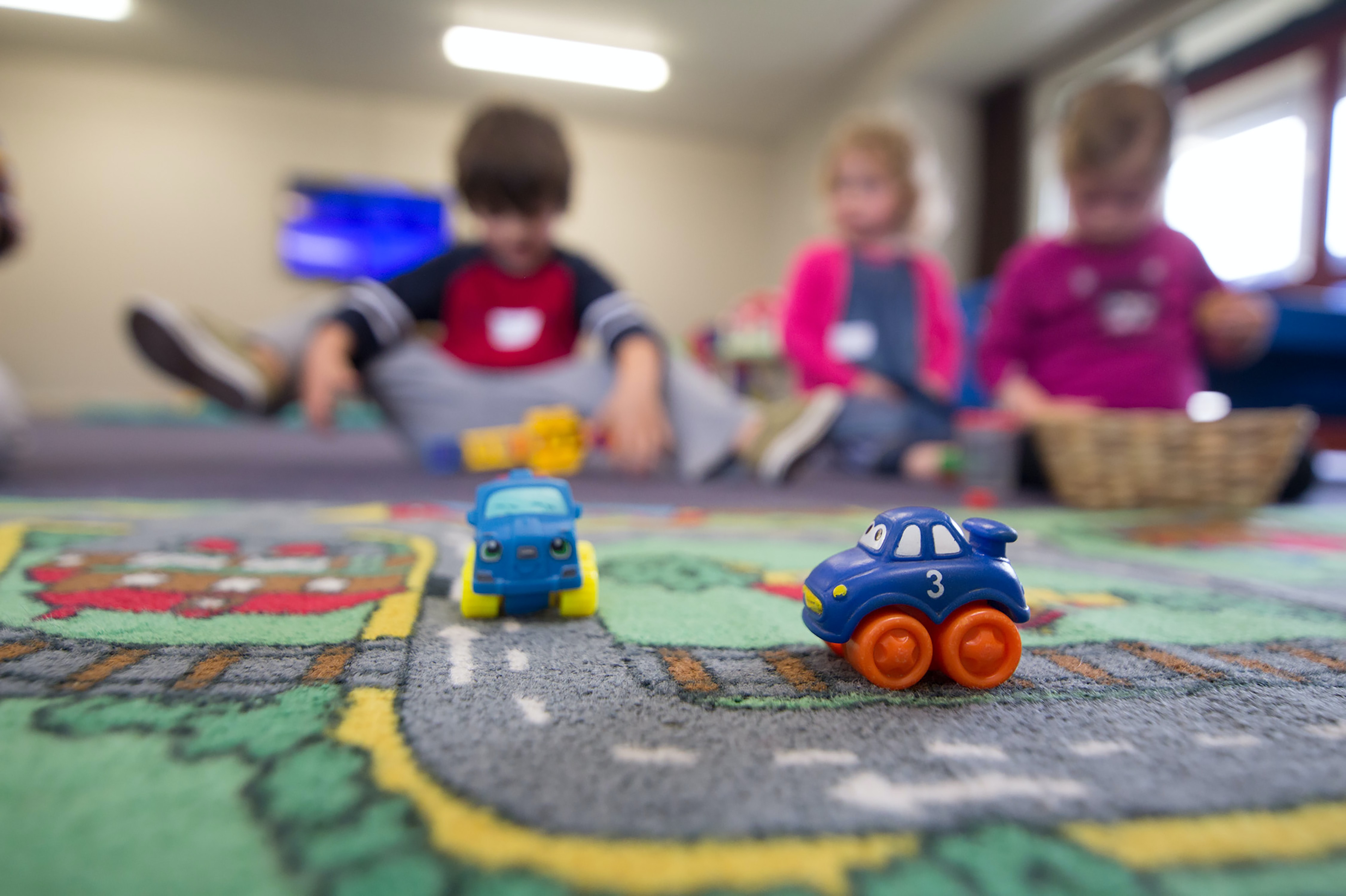 three kids playing with small toy cars at daycare in Sagehill